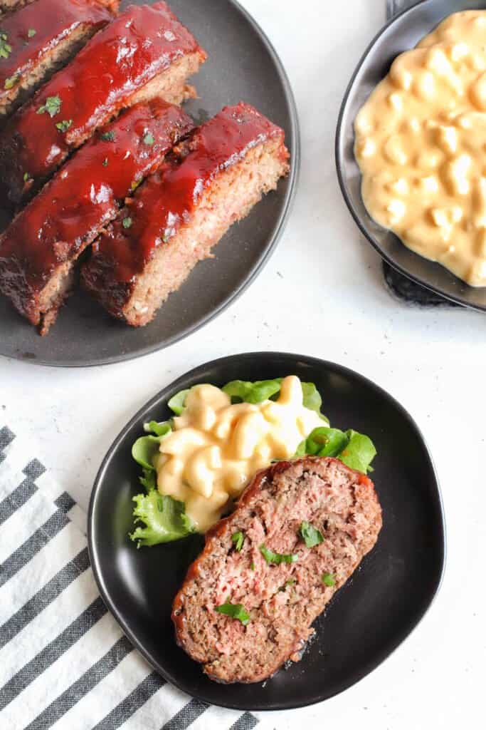 A slice of meatloaf next to the more meatloaf slices and macaroni & cheese.