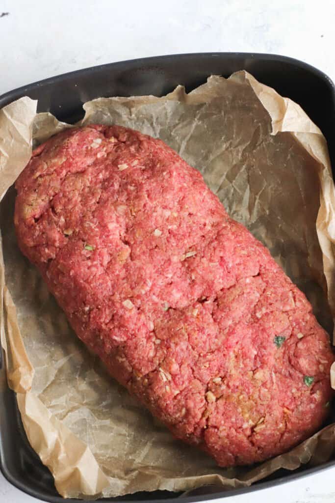 A loaf of seasoned ground beef on parchment paper ready to go into the air fryer.
