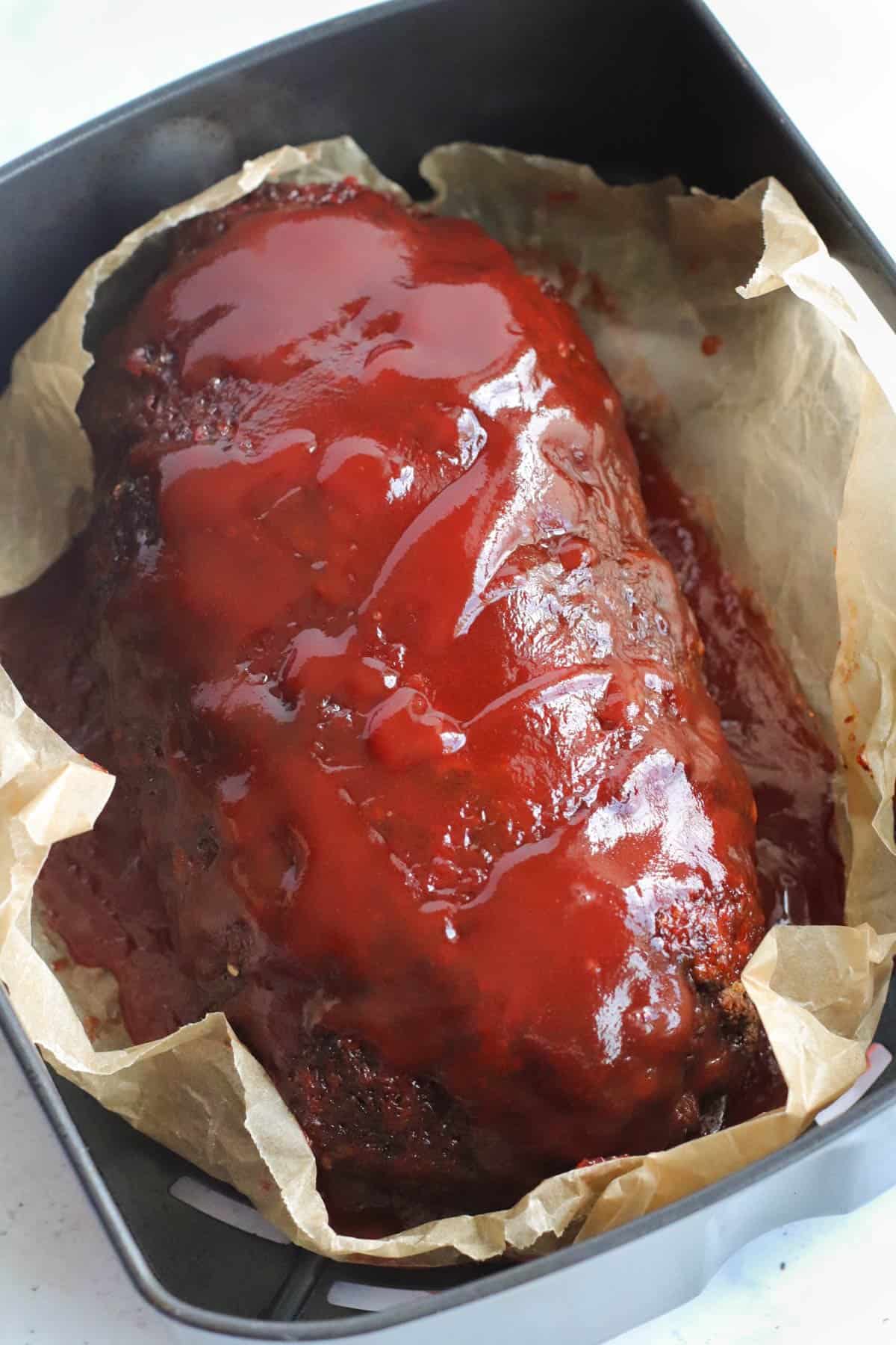 A meatloaf in an air fryer with ketchup glaze.