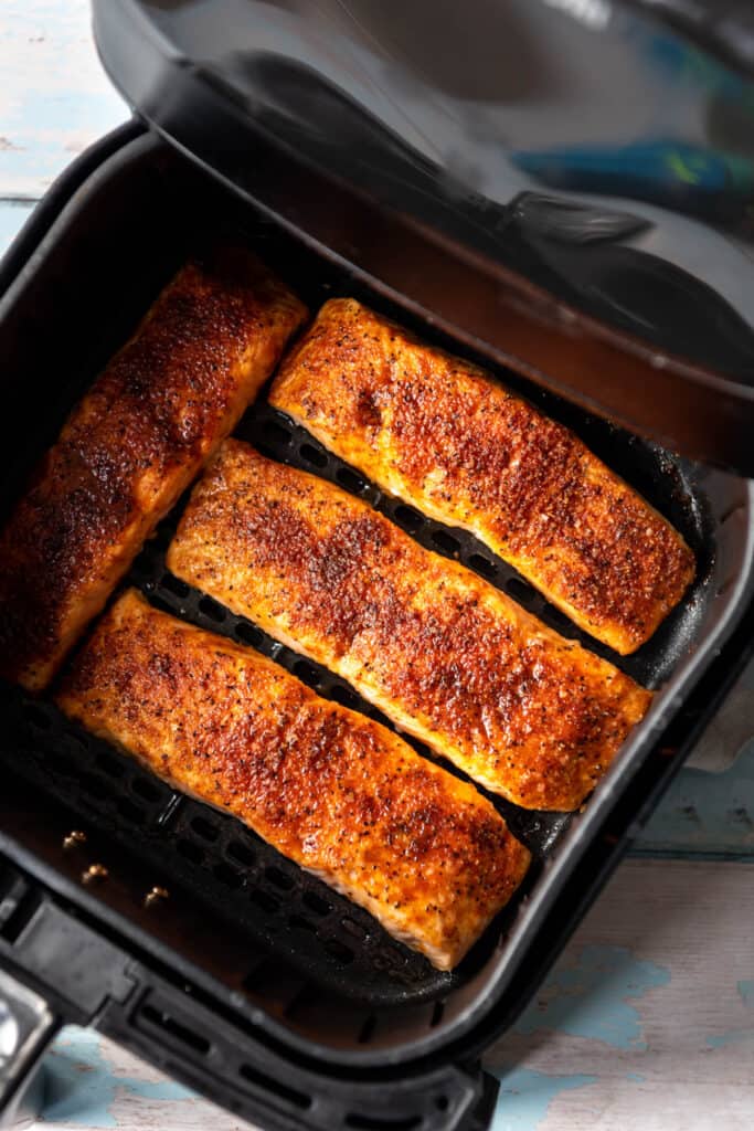 An air fryer basket with four salmon fillets in it.