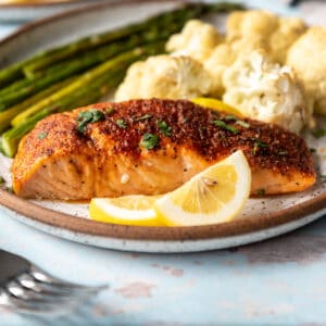 A piece of salmon cooked in the air fryer on a plate with lemon slices.