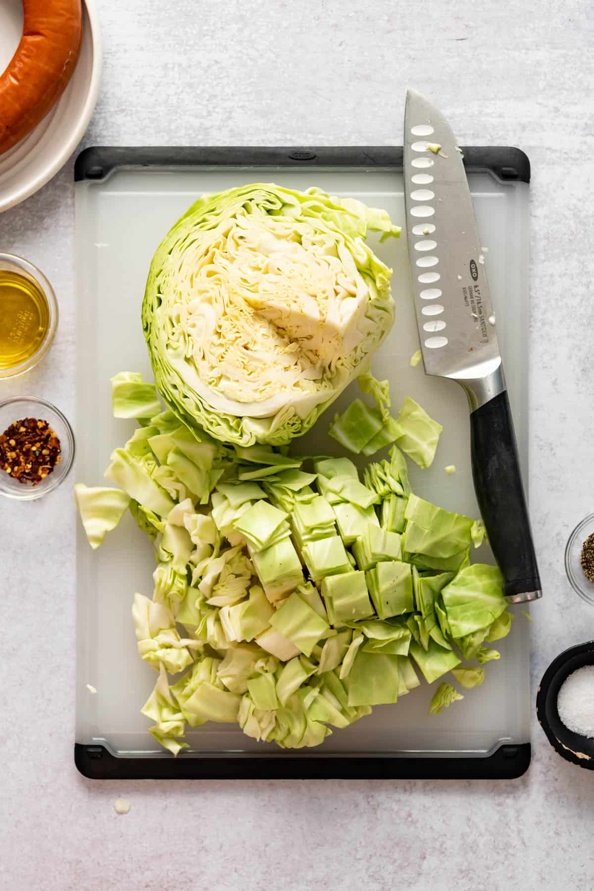 Half a head of green cabbage next to chopped cabbage with a knife on a cutting board.