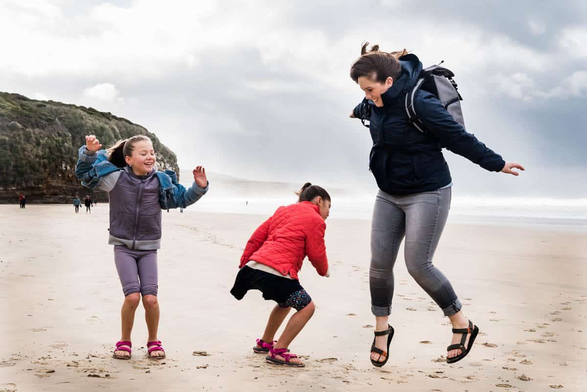 A mom and two girls jumping on a beach.