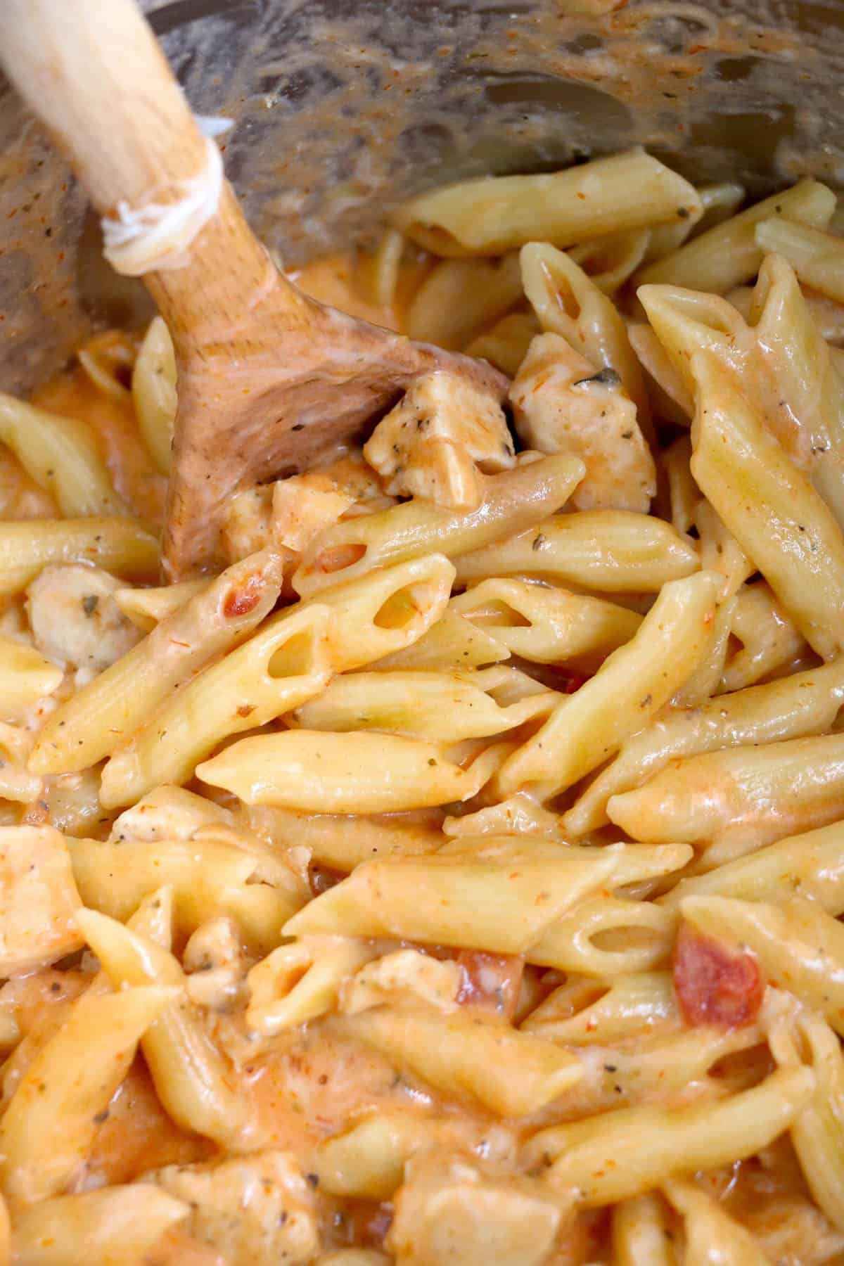 Stirring cooked pasta, chicken, and sauce together with a wooden spoon.