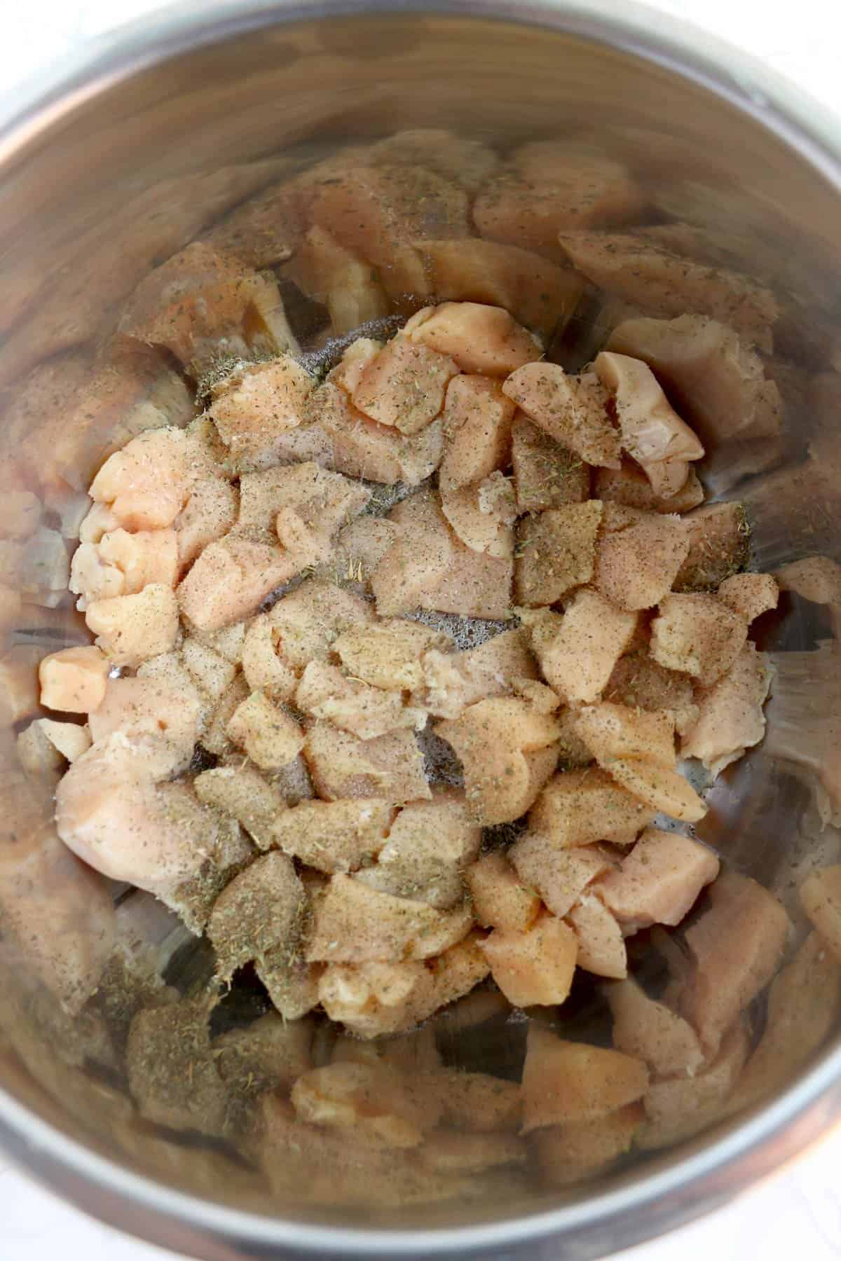 Adding raw chicken chunks with seasoning to the Instant Pot to saute.