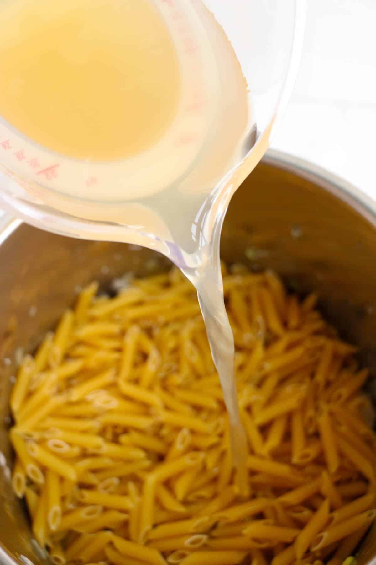 Adding chicken broth to penne pasta in the instant pot.