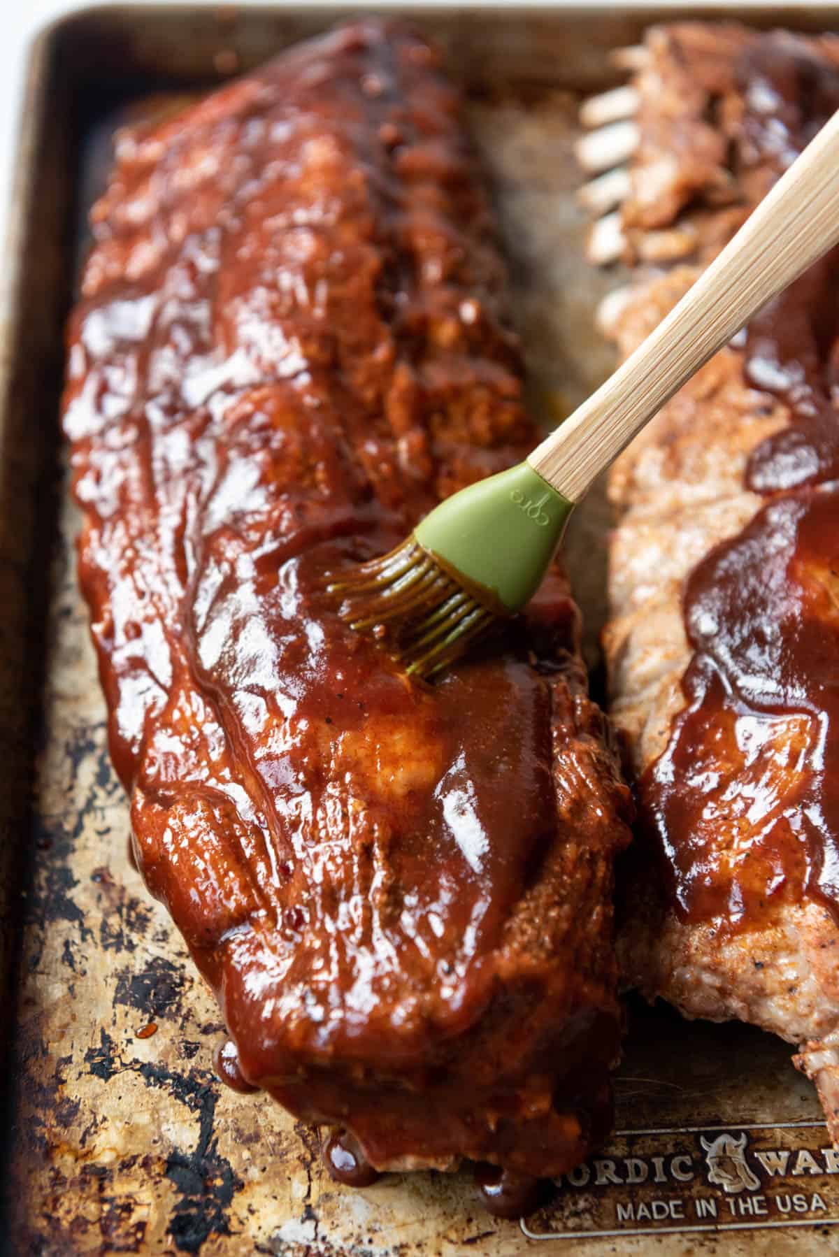 Brushing barbecue sauce onto baby back ribs.
