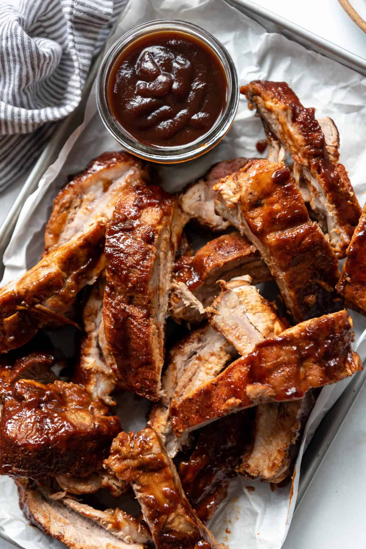 A pile of bbq baby back ribs next to a jar of sauce.