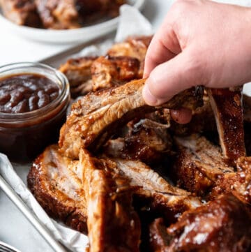 A hand picking up a juicy Instant Pot baby back rib from a pile of ribs.
