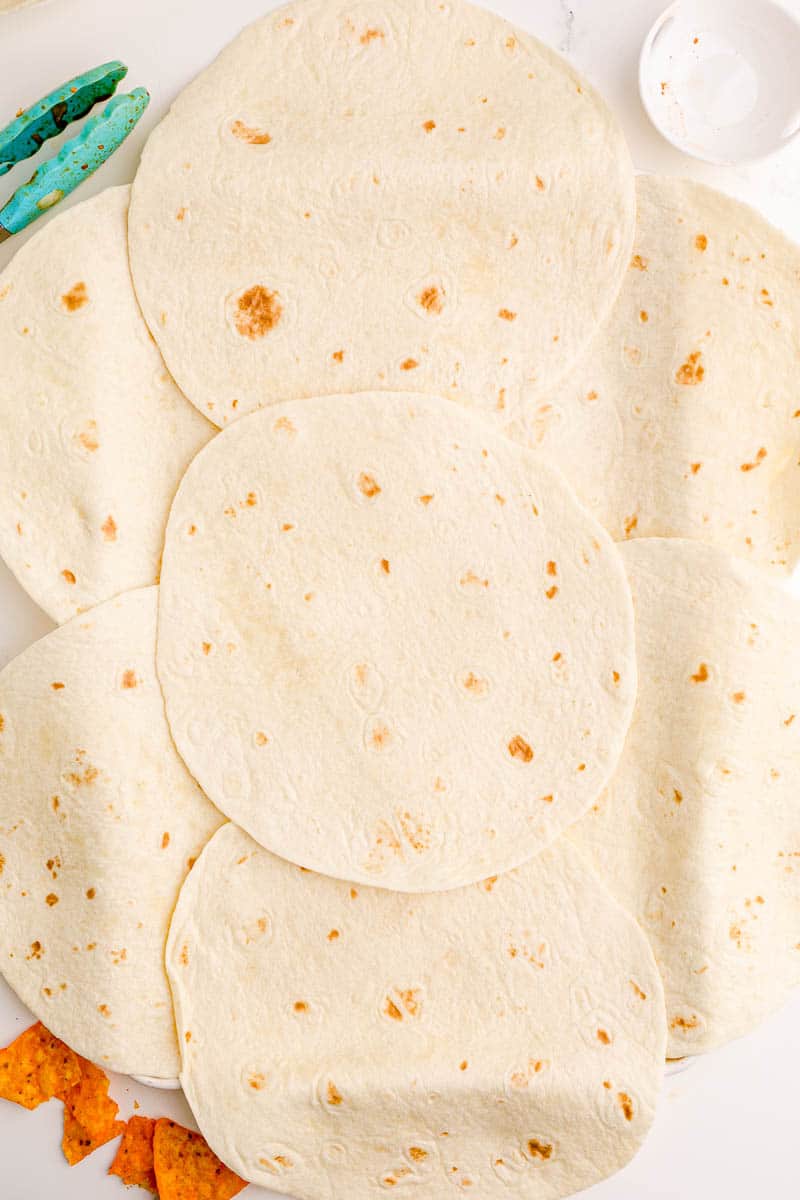 Overlapping and overhanging large flour tortillas on a baking sheet.