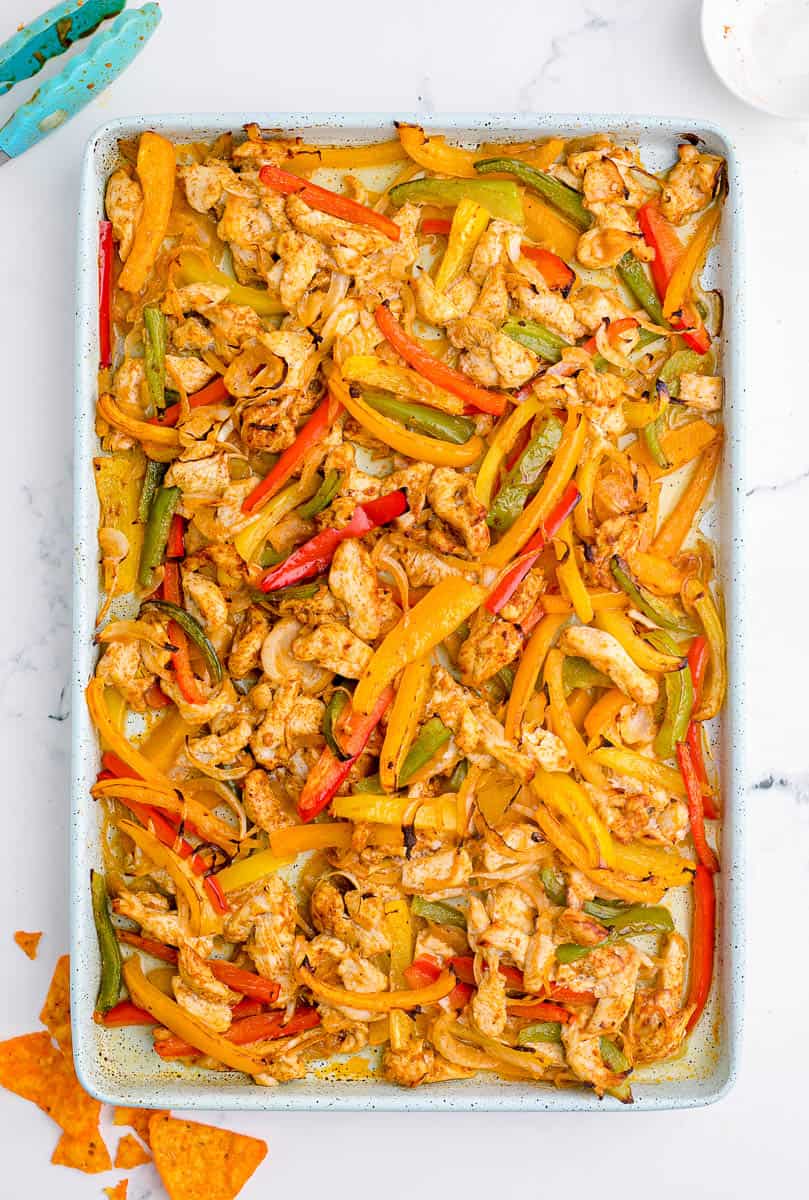 Cooked chicken and bell peppers in a baking sheet.