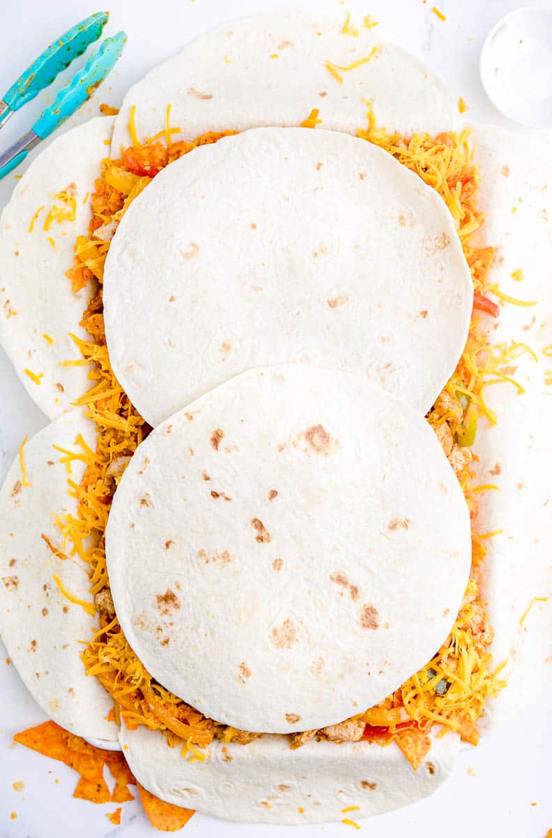 Tortillas arranged on a sheet pan to cover chicken and vegetable filling and cheese.