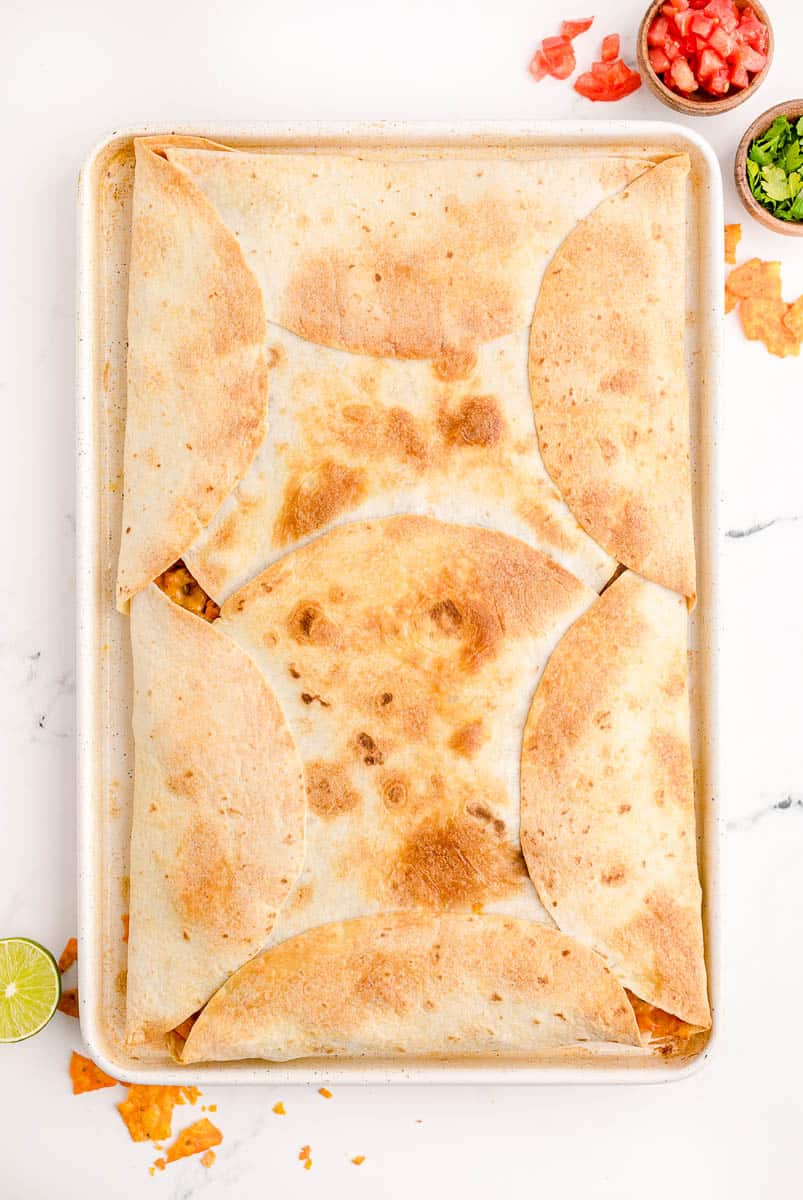 Baked quesadillas on a large sheet pan just out of the oven.