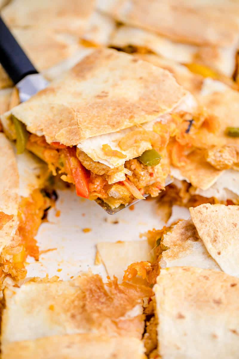 A spatula lifting a slice of baked chicken quesadilla from the pan.