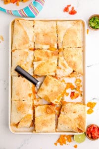 Oven quesadillas cut into squares on a baking dish with a spatula.
