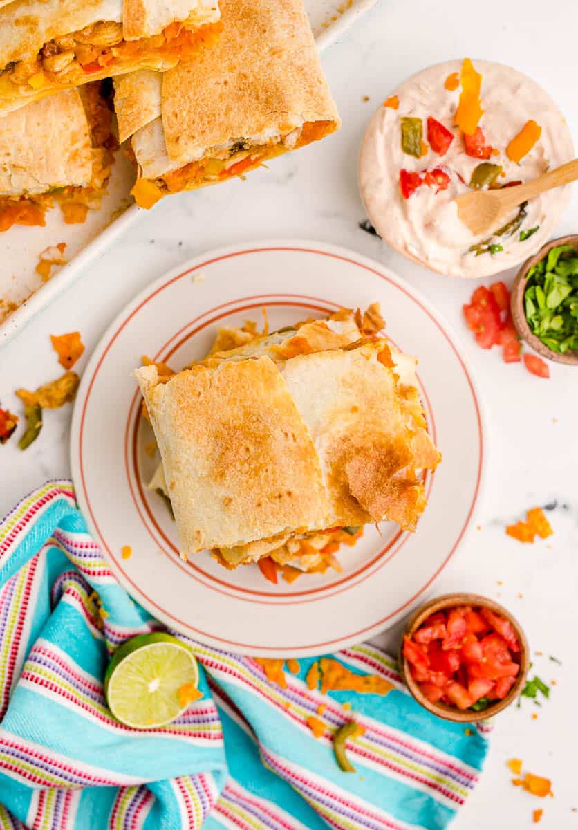 An oven baked quesadilla on a white plate next to toppings.