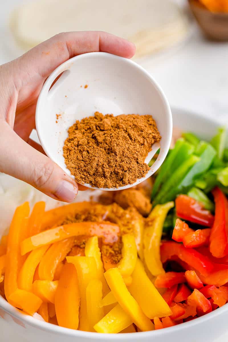 Sprinkling taco seasoning over sliced bell peppers.