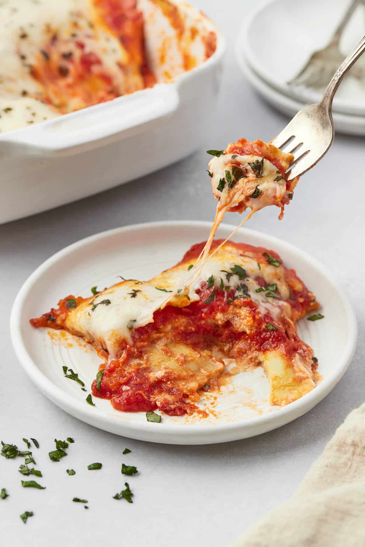 A fork lifting a bite of ravioli lasagna from a plate.