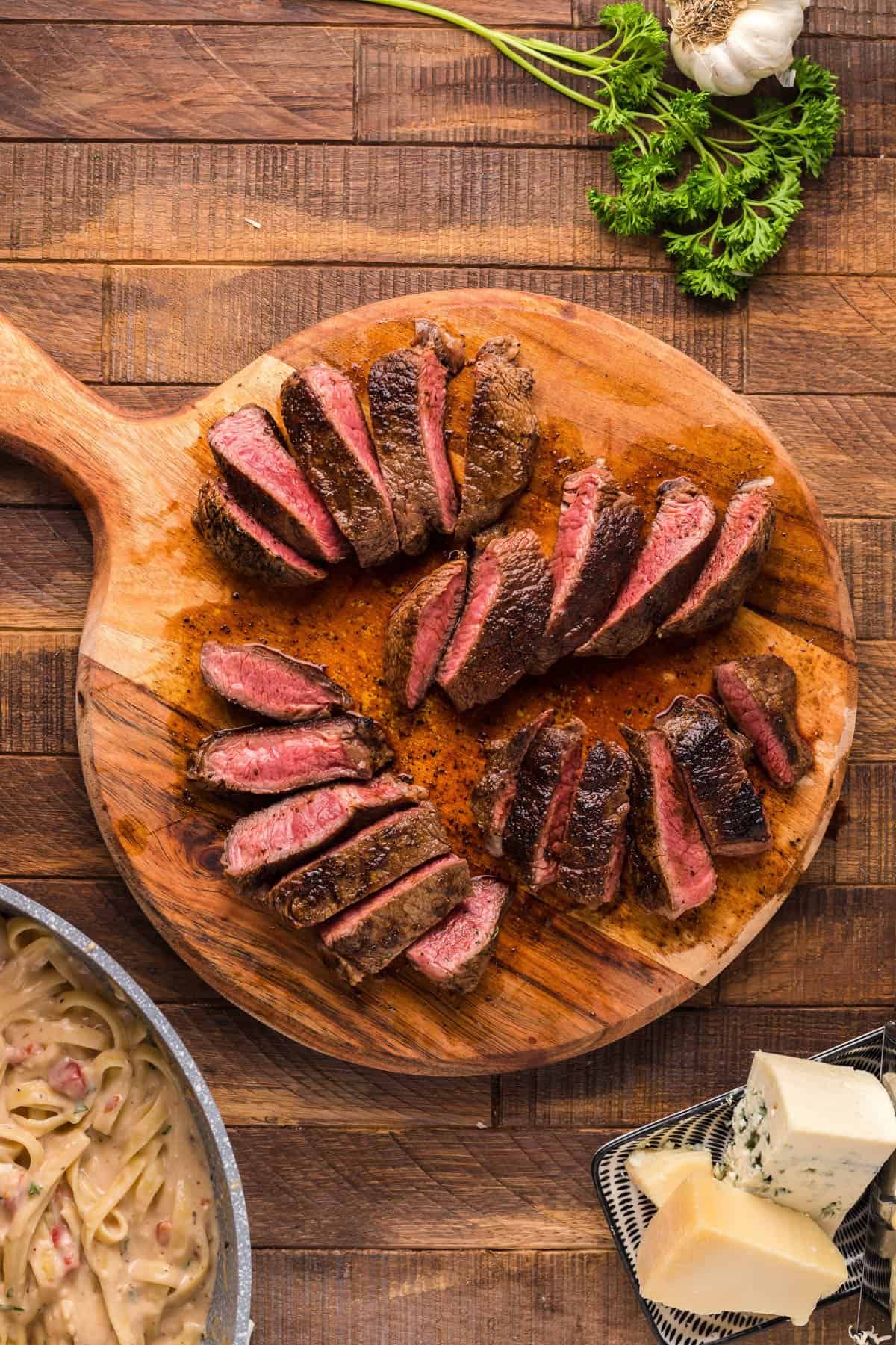 Cook steak sliced into strips on a round wooden cutting board.