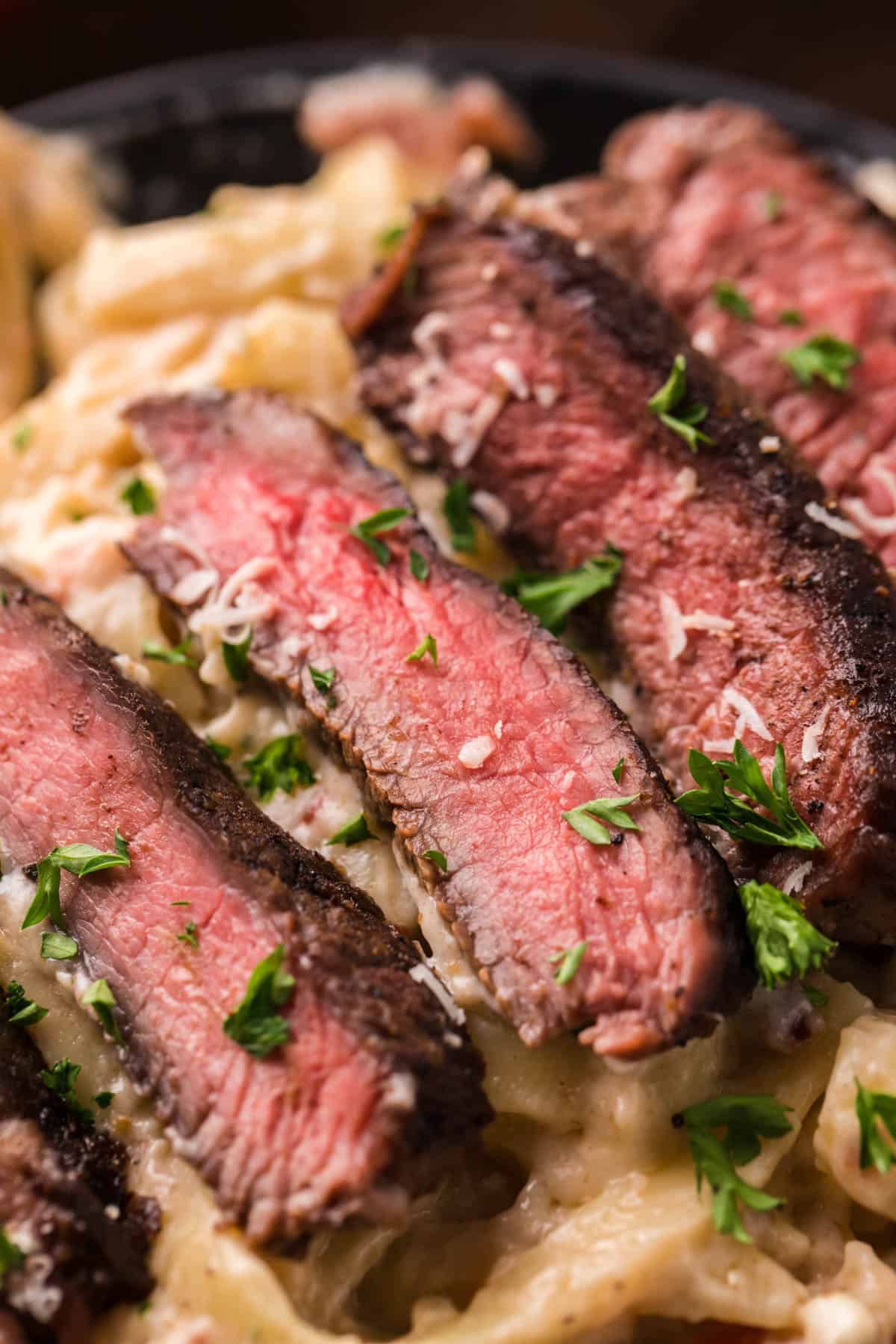 A close image of perfectly seared medium rare steak alfredo pasta.