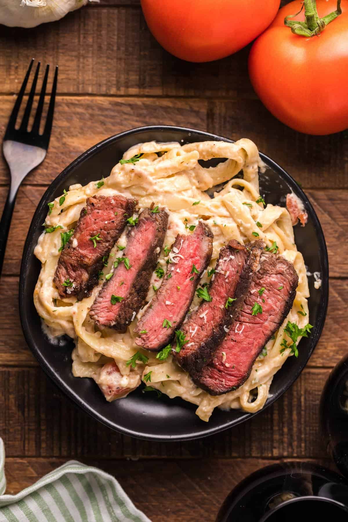 A plate of steak alfredo next to tomatoes and a fork.