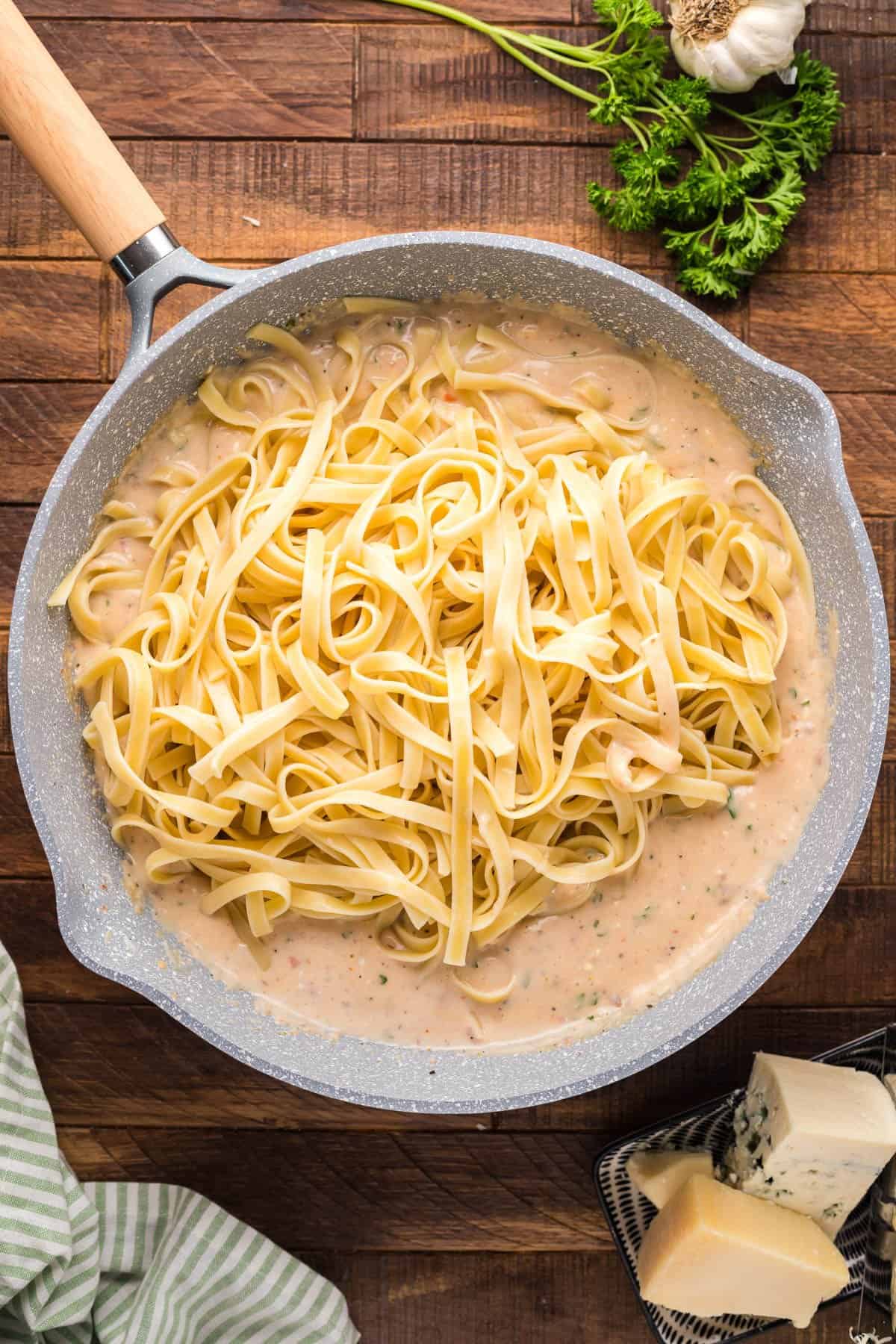 Adding cooked and drained fettuccine pasta to alfredo sauce in a large pan.