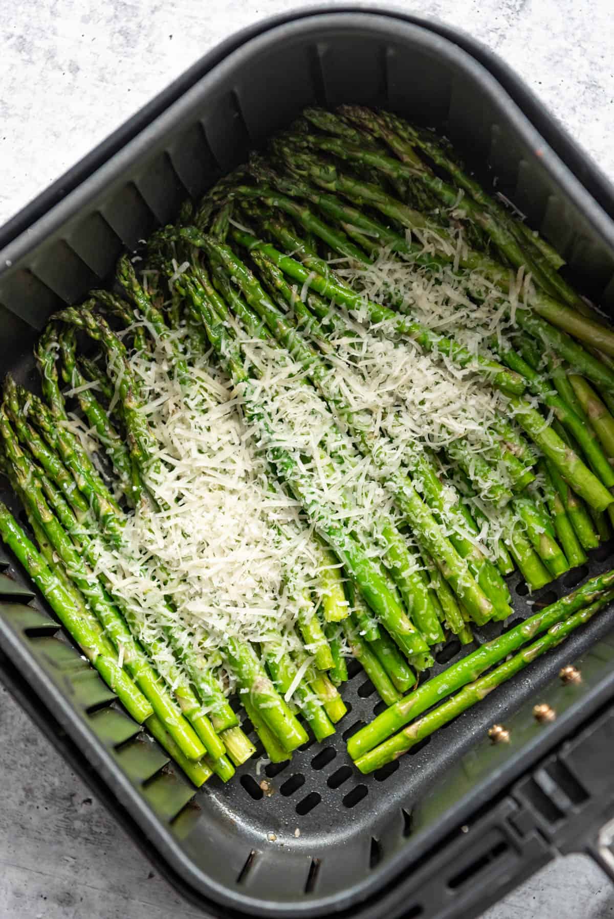 Asparagus in the air fryer with freshly grated parmesan sprinkled on top.