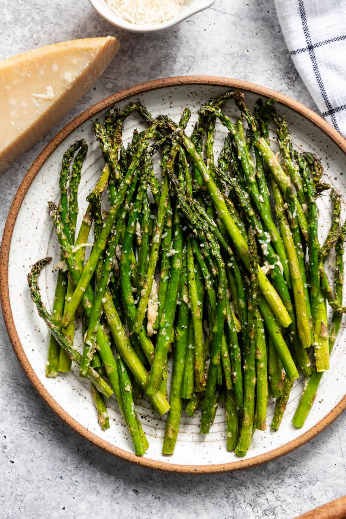 A plate of roasted air fryer asparagus next to parmesan cheese.