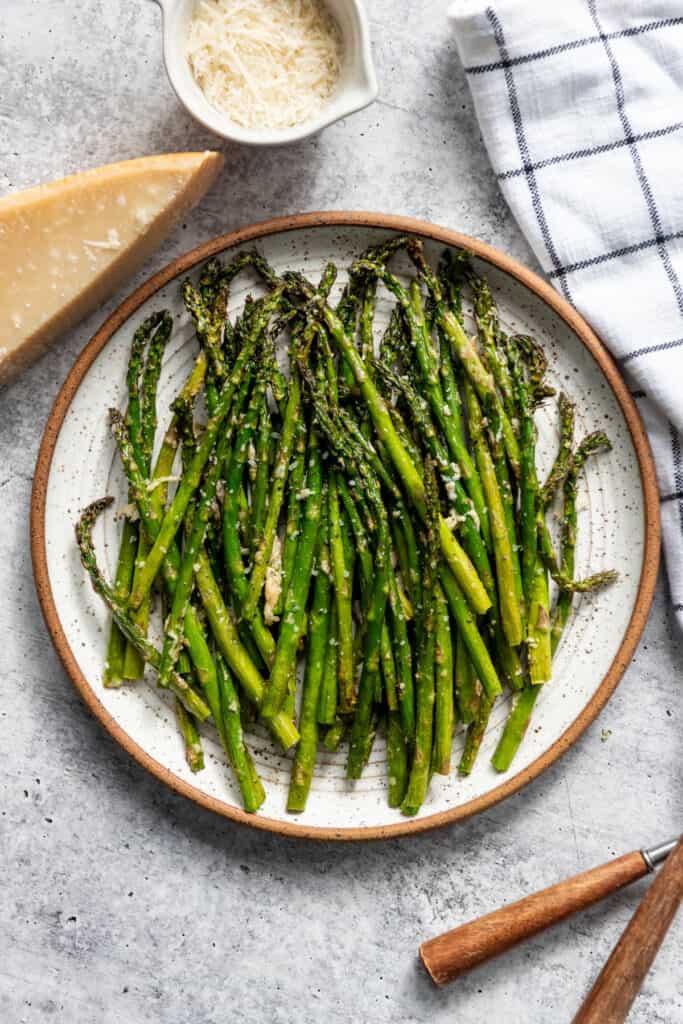 A plate of roasted air fryer asparagus next to parmesan cheese.