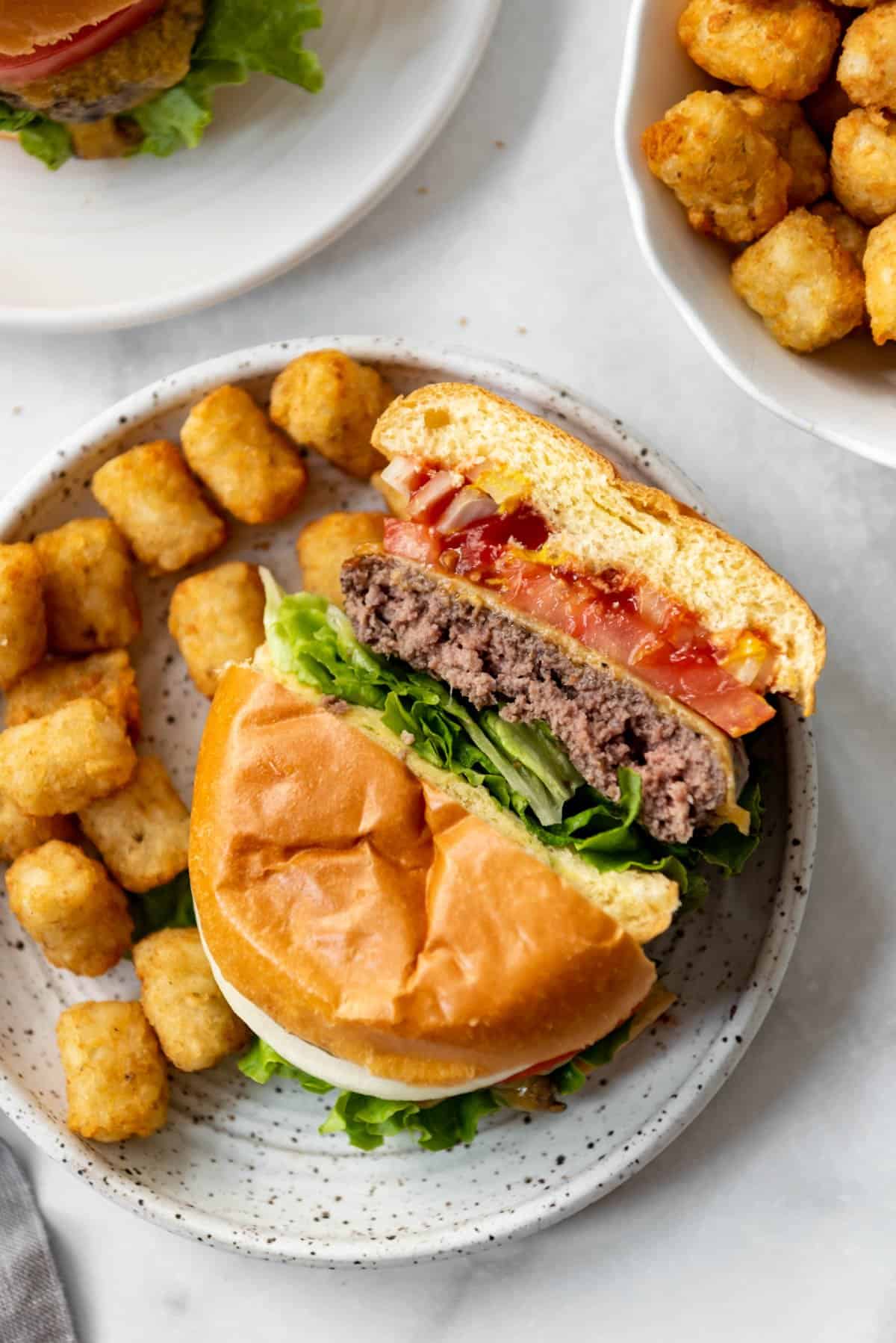 An air fryer hamburger cut in half on a plate with tater tots.