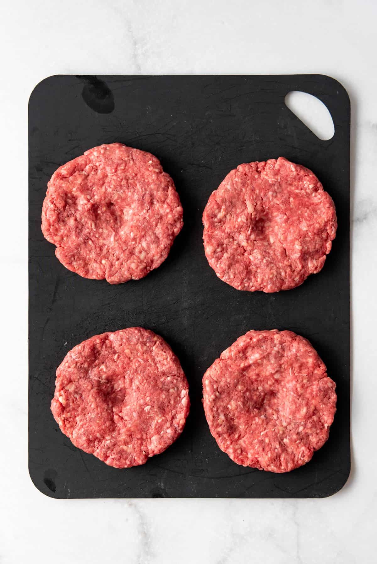 Four homemade hamburger patties with indents in the top of each patty.
