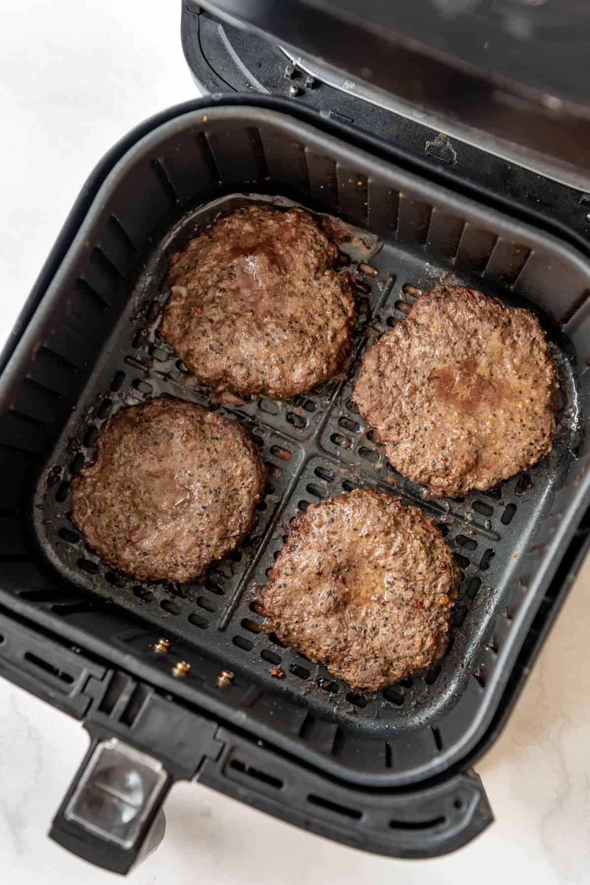 Cooked hamburgers in an air fryer basket.