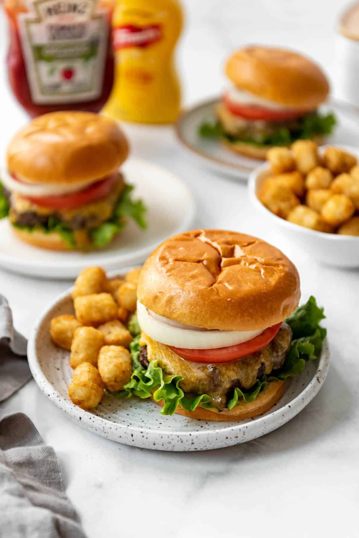 Hamburgers made in the air fryer on plates with tater tots next to jars of ketchup and mustard.