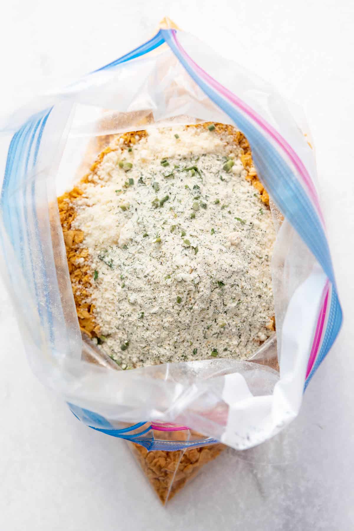 Adding homemade ranch seasoning to crushed cornflakes in a Ziploc bag.