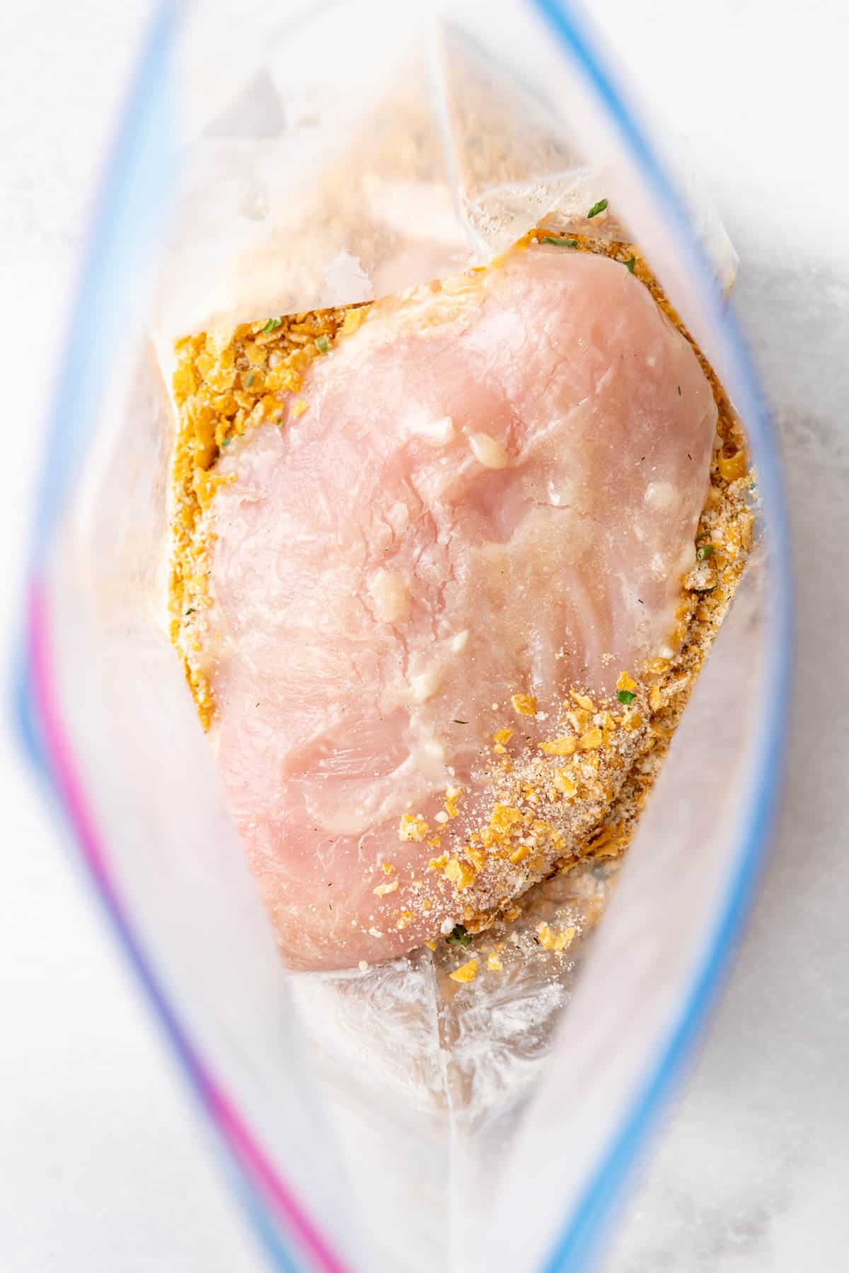 A chicken breast in a resealable bag filled with ranch seasoned crushed cornflakes.