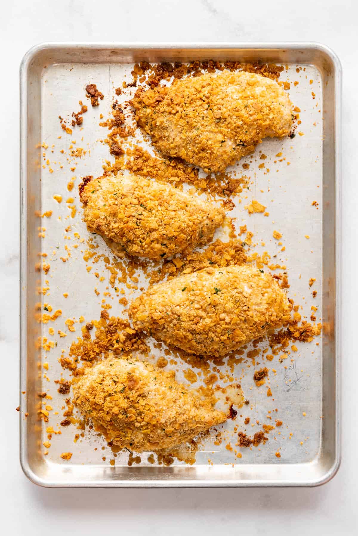 Four baked ranch chicken breasts on a baking sheet.
