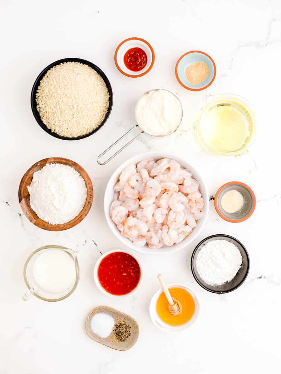 Raw shrimp, panko breadcrumbs, flour, cornstarch and the rest of the ingredients on a marble countertop