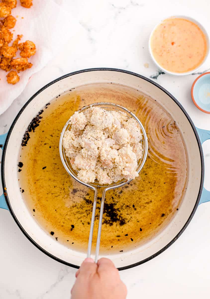 A spider utensil holding uncooked, breaded shrimp over a pot of hot oil