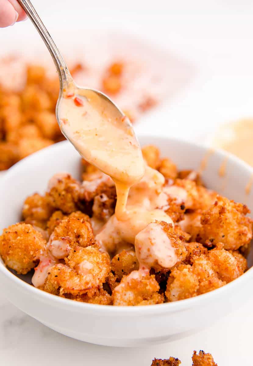 Breaded shrimp in a bowl with bang bang sauce being spooned on top of the shrimp