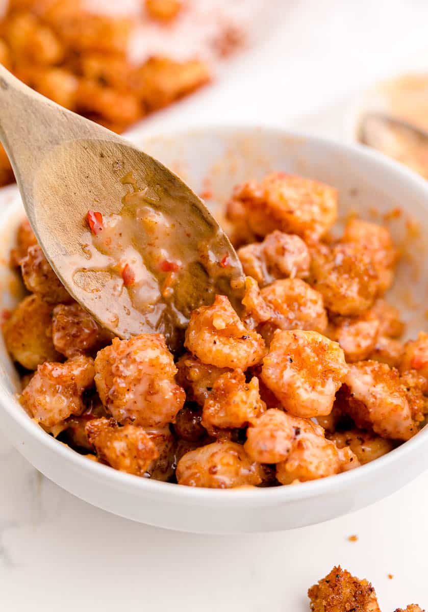 A wooden spoon combining breaded shrimp with homemade bang bang sauce