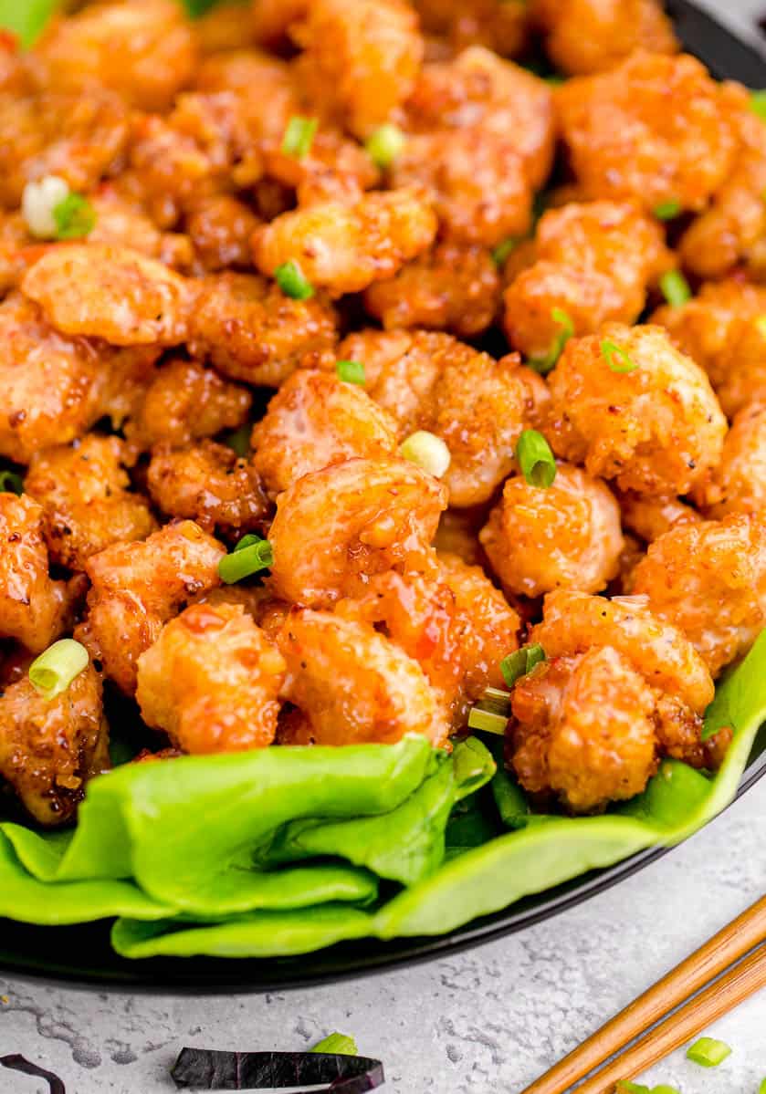 A large black bowl holding a bed of lettuce with a batch of bang bang shrimp on top