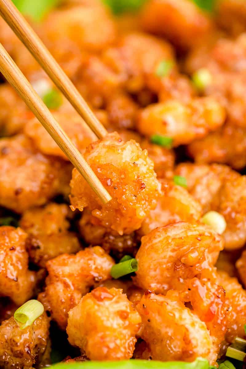 A bang bang shrimp being lifted from a bowl by a pair of wooden chopsticks