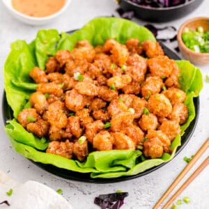 Bang bang shrimp in a large bowl with bang bang sauce and purple cabbage in the background