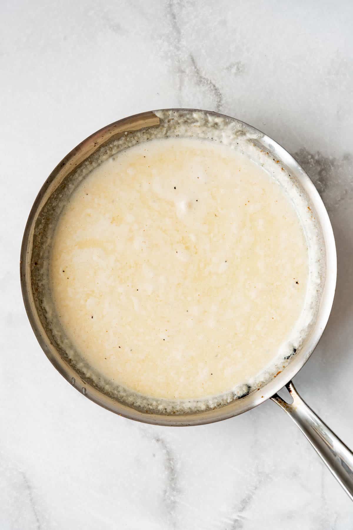 Simmered cream, butter, garlic, and spices in a pan for homemade alfredo sauce.