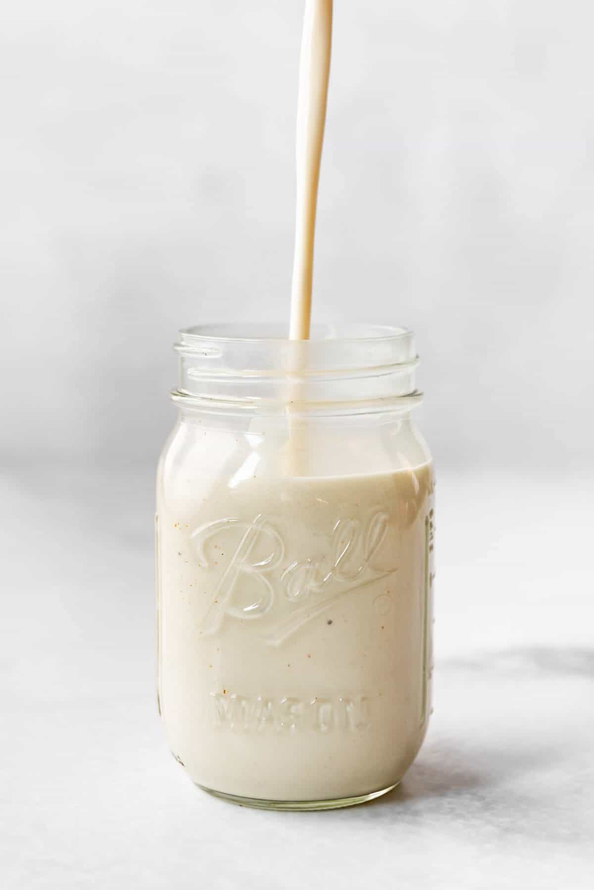 Homemade alfredo sauce being poured into a glass mason jar.