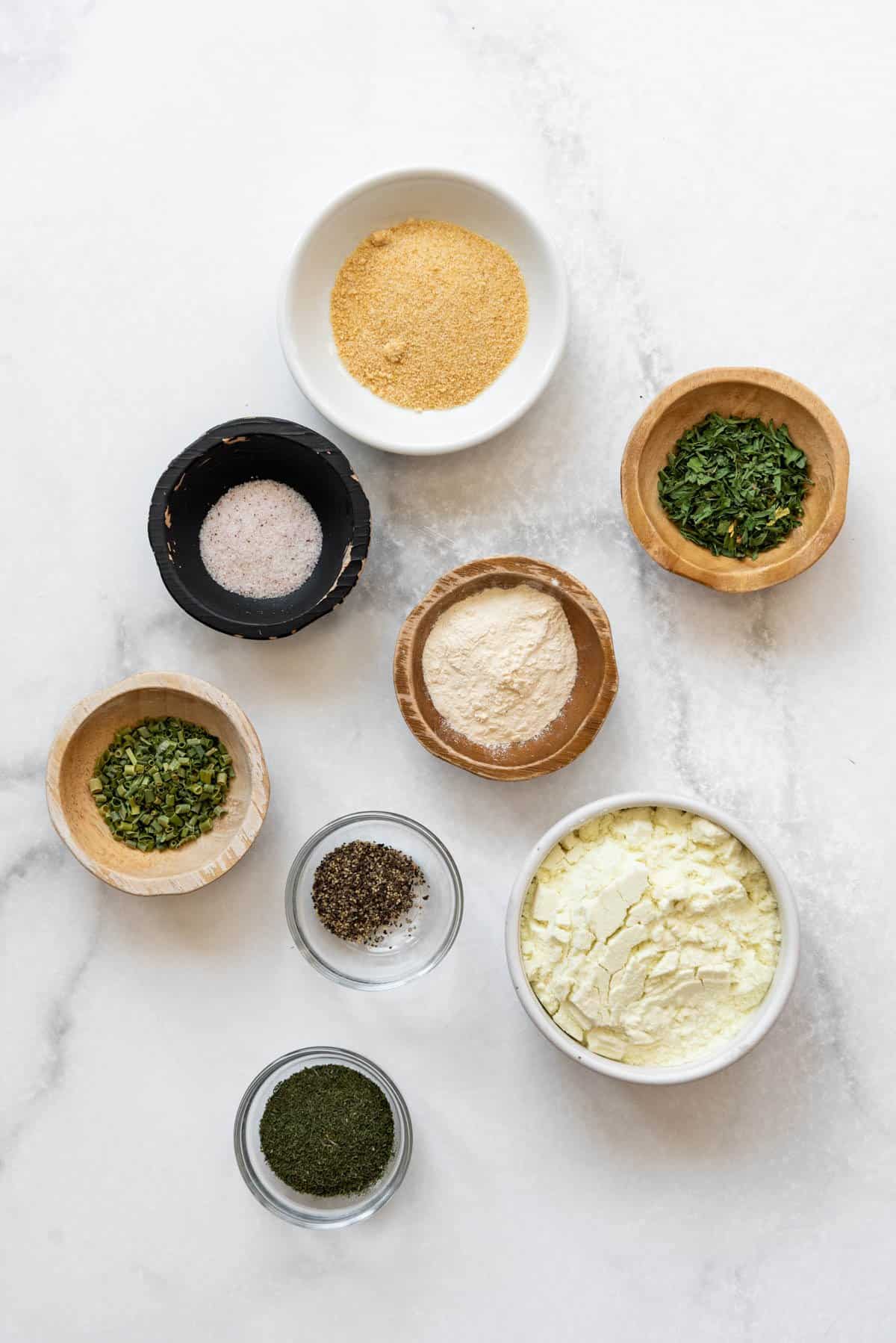 Ingredients for making homemade ranch seasoning in separate bowls on a white surface.