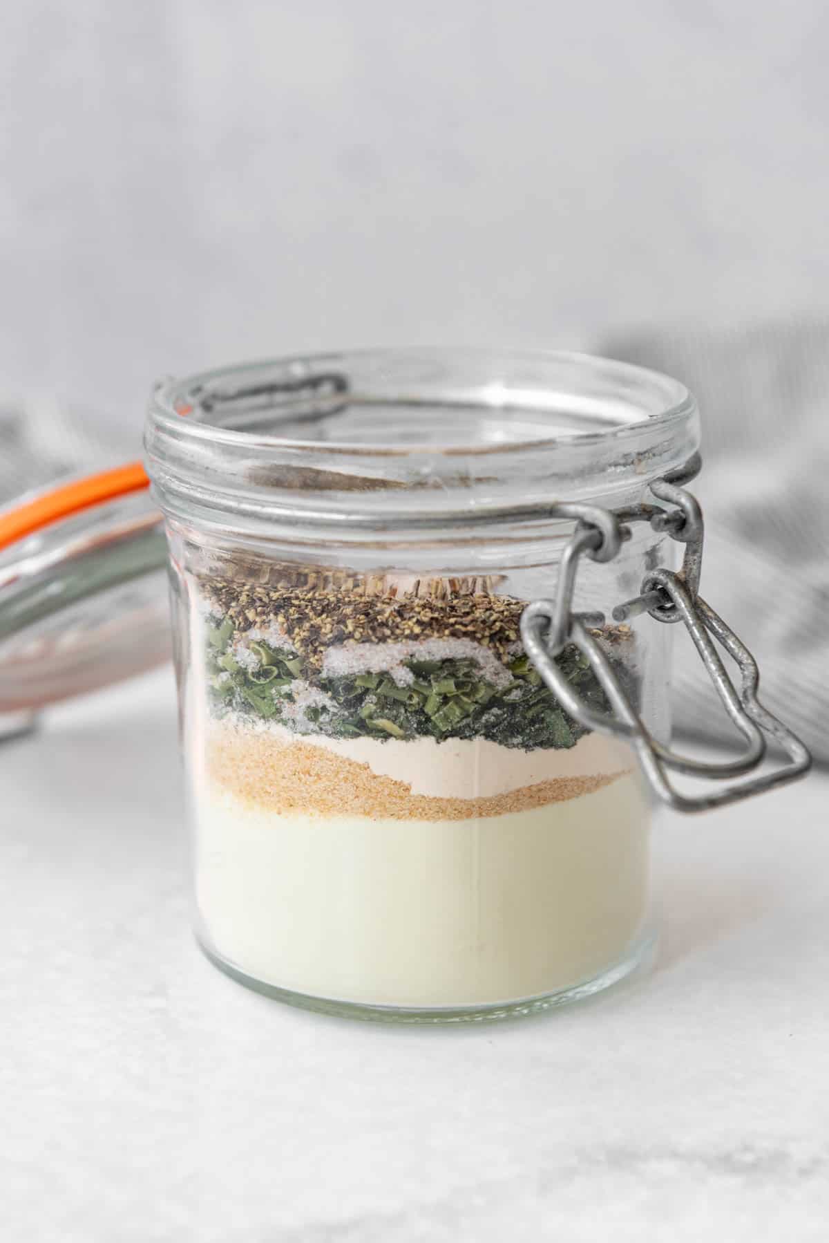 Layered ingredients for making homemade ranch seasoning in a glass jar.