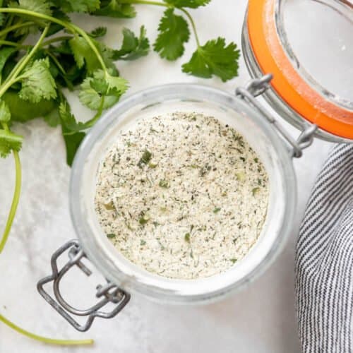 A glass jar filled with homemade ranch seasoning mix next to green herbs.