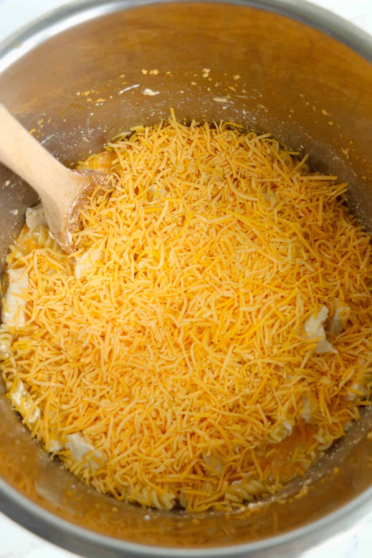 Adding shredded cheddar cheese to other ingredients in the instant pot.
