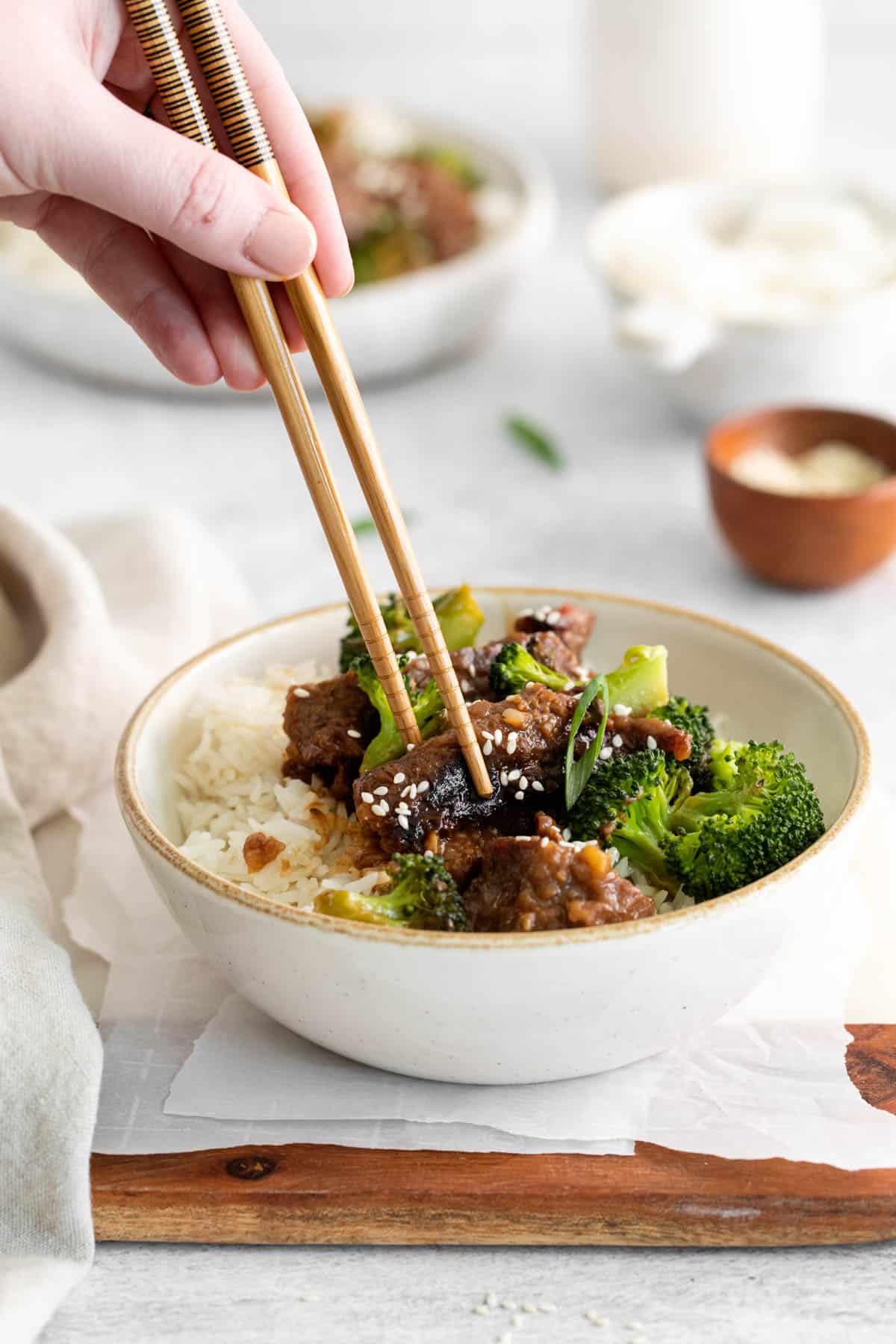 A hand using chopsticks to lift a piece of Mongolian beef from a bowl.